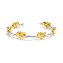 Load image into Gallery viewer, Two-tone knot cuff bracelet with polished gold knots on a silver open bangle, showcasing a contemporary mixed metal design for everyday wear, layering, and minimalist styling.
