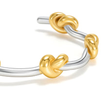 Load image into Gallery viewer, Close-up of a two-tone knot cuff bracelet featuring polished gold knot accents intertwined on a sleek silver open bangle with a modern minimalist mixed metal design.
